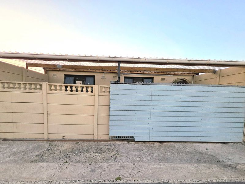 Front exterior view of the property featuring a precast concrete boundary wall, sliding gate, and a covered carport area.