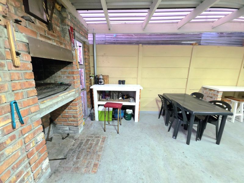 Covered outdoor patio area featuring a built-in brick braai, concrete flooring, and a functional prep counter, ideal for outdoor entertaining.