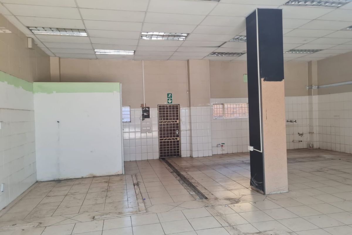 An empty commercial utility space featuring tiled flooring, suspended ceilings with recessed lighting, and functional wall tiling, suitable for various business or storage applications.