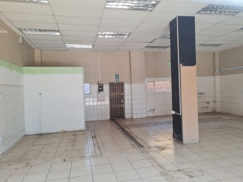 An empty commercial utility space featuring tiled flooring, suspended ceilings with recessed lighting, and functional wall tiling, suitable for various business or storage applications.