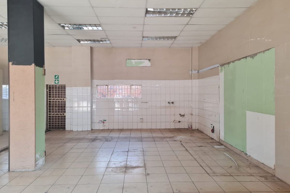An empty, open-plan commercial space featuring tiled flooring, a suspended ceiling with recessed lighting, and a tiled wall section, requiring cosmetic refurbishment.