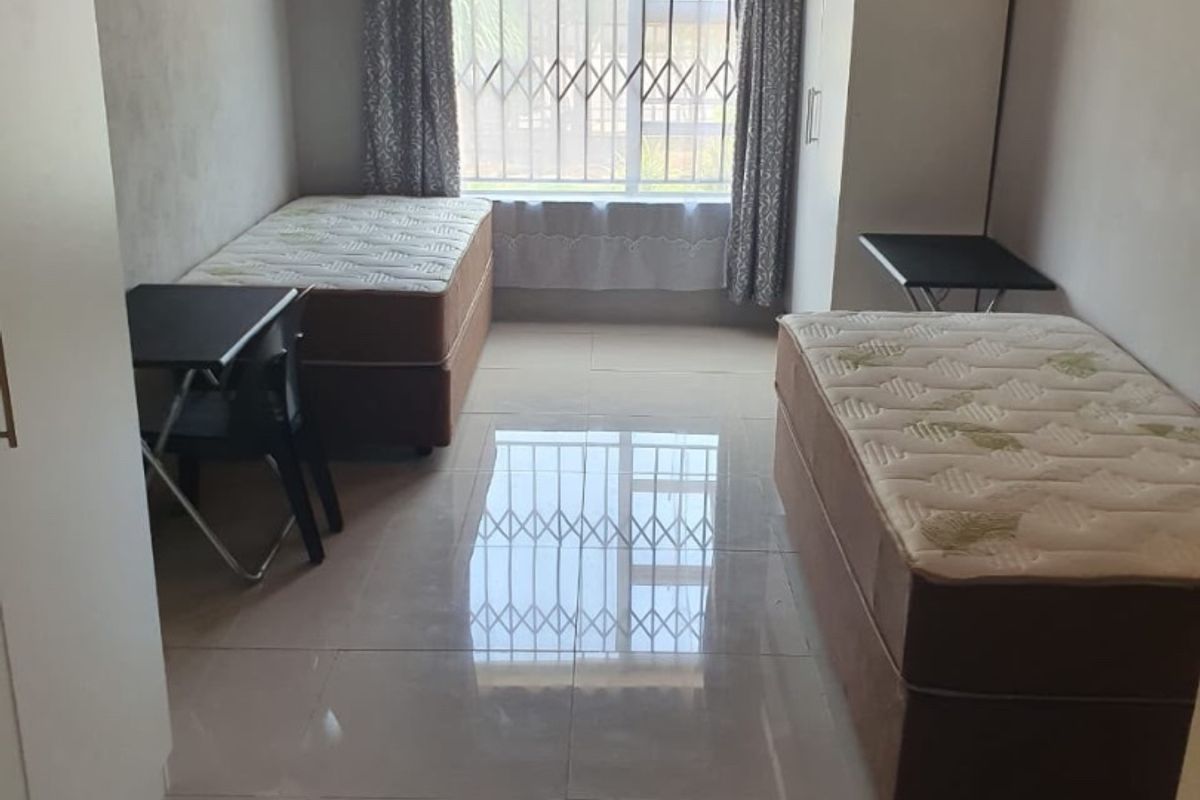 A functional bedroom featuring tiled flooring, security bars on the window, and a timber ceiling.