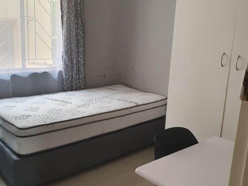 A compact bedroom featuring tiled flooring, a built-in wardrobe, and a window fitted with security bars.