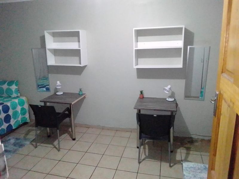 A functional bedroom space featuring tiled flooring and wall-mounted shelving units, suitable for a study or sleeping area.