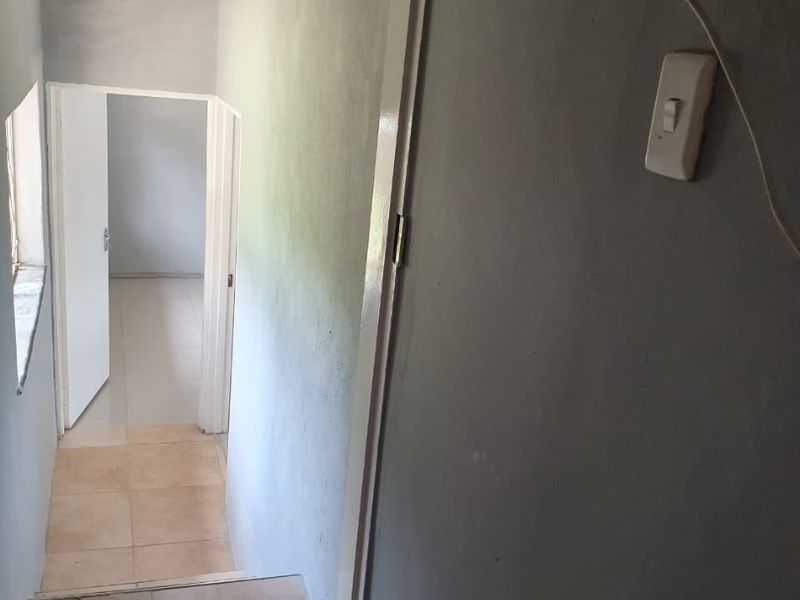 A narrow hallway featuring tiled flooring and basic lighting, leading into an adjacent room. The space requires cosmetic updates to the wall finishes.