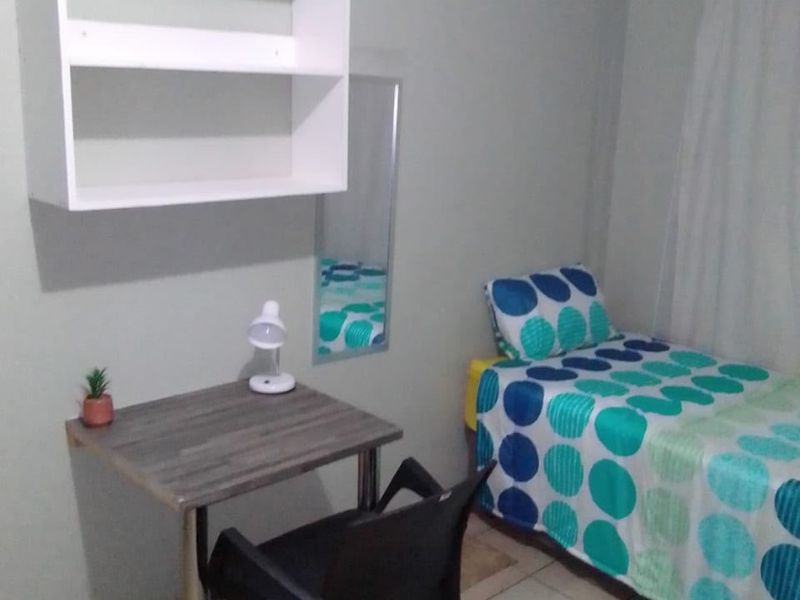A compact bedroom featuring tiled flooring, built-in wall shelving, and a curtain rail, providing a functional living space.