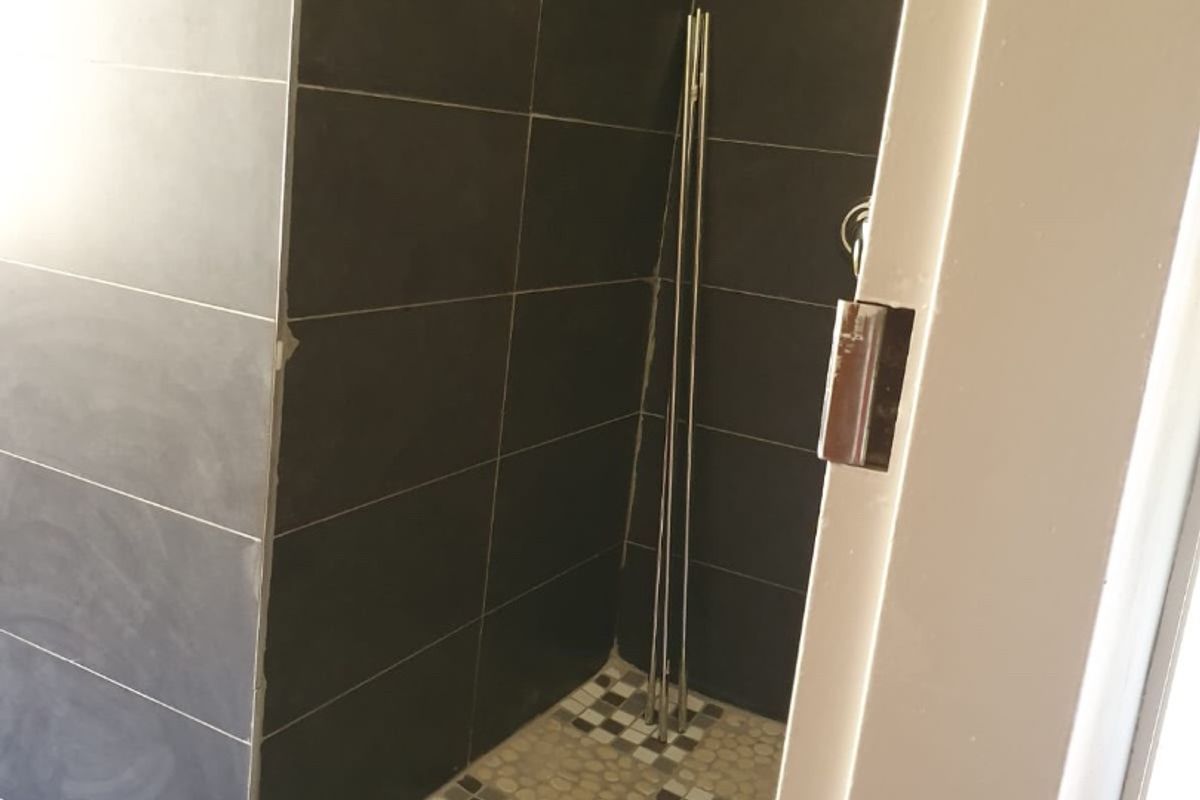 A partially finished walk-in shower featuring dark wall tiles and mosaic floor tiling, currently awaiting final trim and finishing touches.