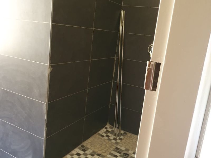A partially finished walk-in shower featuring dark wall tiles and mosaic floor tiling, currently awaiting final trim and finishing touches.
