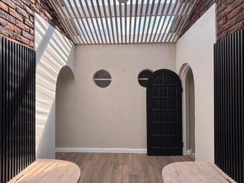 A modern, covered patio area featuring exposed brick walls, a slatted pergola roof, arched entryways, and stylish vertical slat wall detailing.
