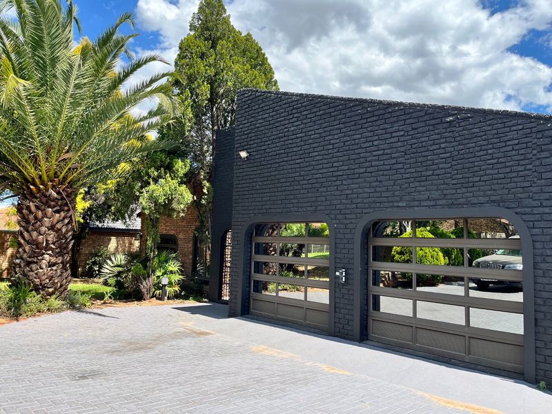 A modern double garage with a dark brick facade and paved driveway, featuring contemporary glass-panelled garage doors.
