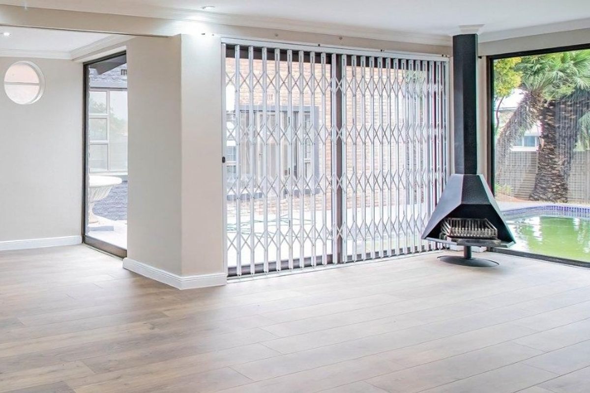 Spacious living area featuring modern laminate flooring, a contemporary freestanding fireplace, and large sliding glass doors with security gates overlooking the pool area.
