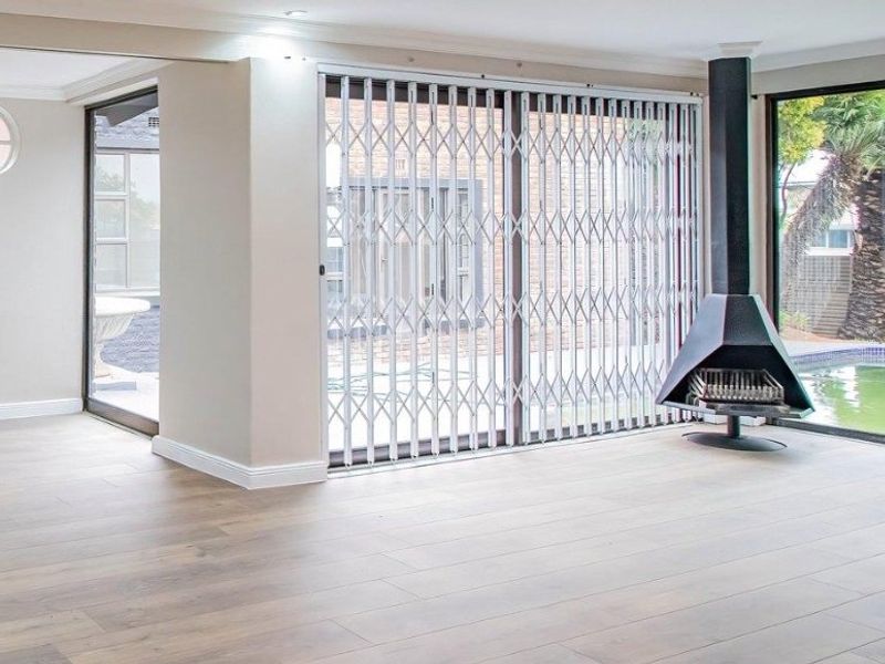 Spacious living area featuring modern laminate flooring, a contemporary freestanding fireplace, and large sliding glass doors with security gates overlooking the pool area.
