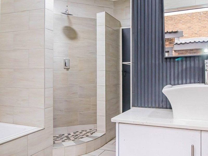 Modern bathroom featuring a walk-in shower with rain shower head, built-in vanity with vessel sink, and tiled finishes throughout.