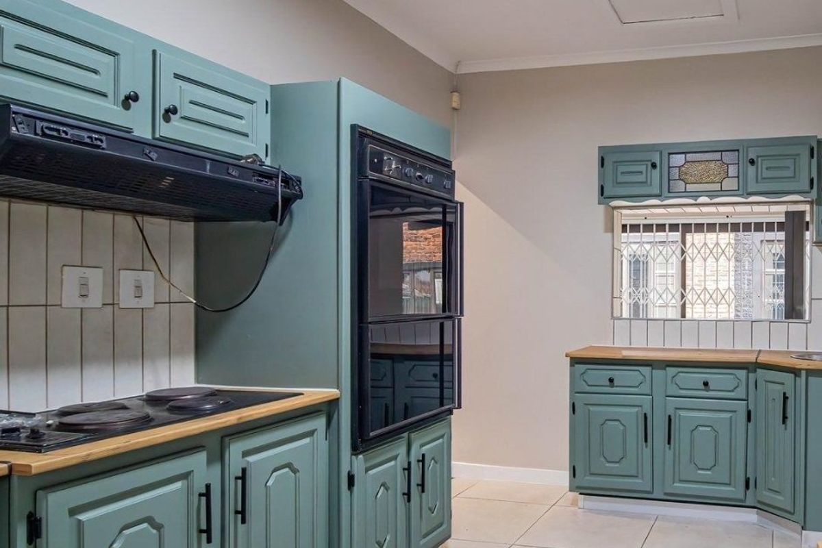 A functional kitchen featuring sage green cabinetry, built-in double oven, electric hob, extractor fan, and tiled flooring with a security-gated window.