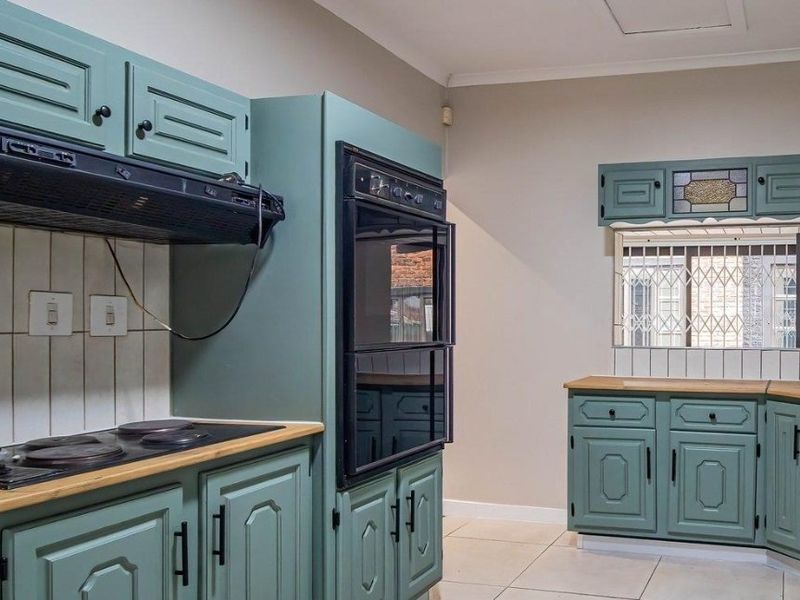 A functional kitchen featuring sage green cabinetry, built-in double oven, electric hob, extractor fan, and tiled flooring with a security-gated window.