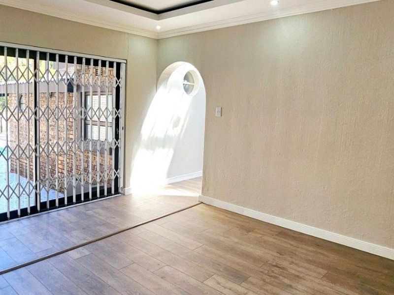 An empty living room featuring laminate flooring, a decorative archway, and a sliding security gate leading to the outdoor area.