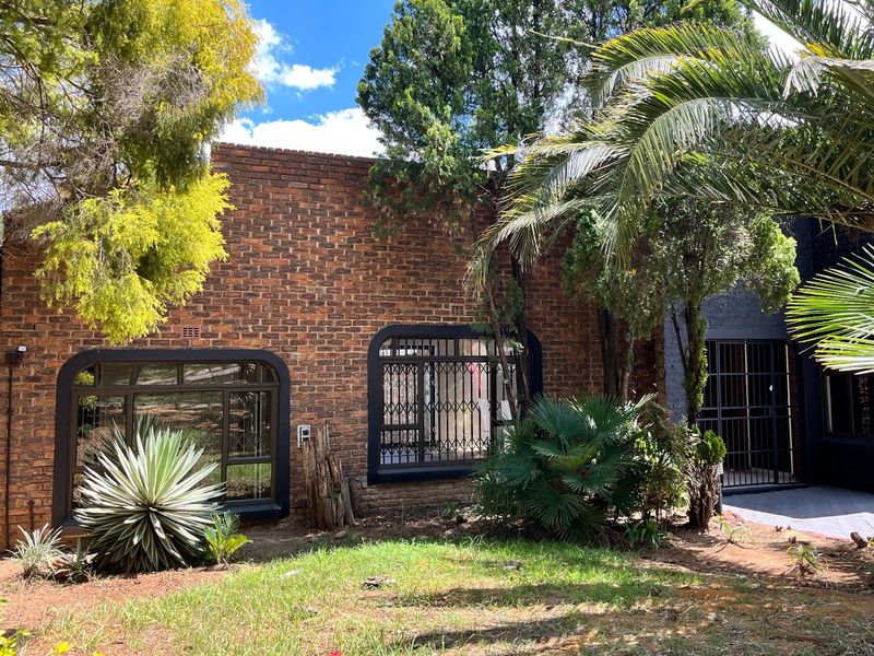 Front elevation of a face brick house featuring dark metal window frames, security bars, and established garden landscaping.