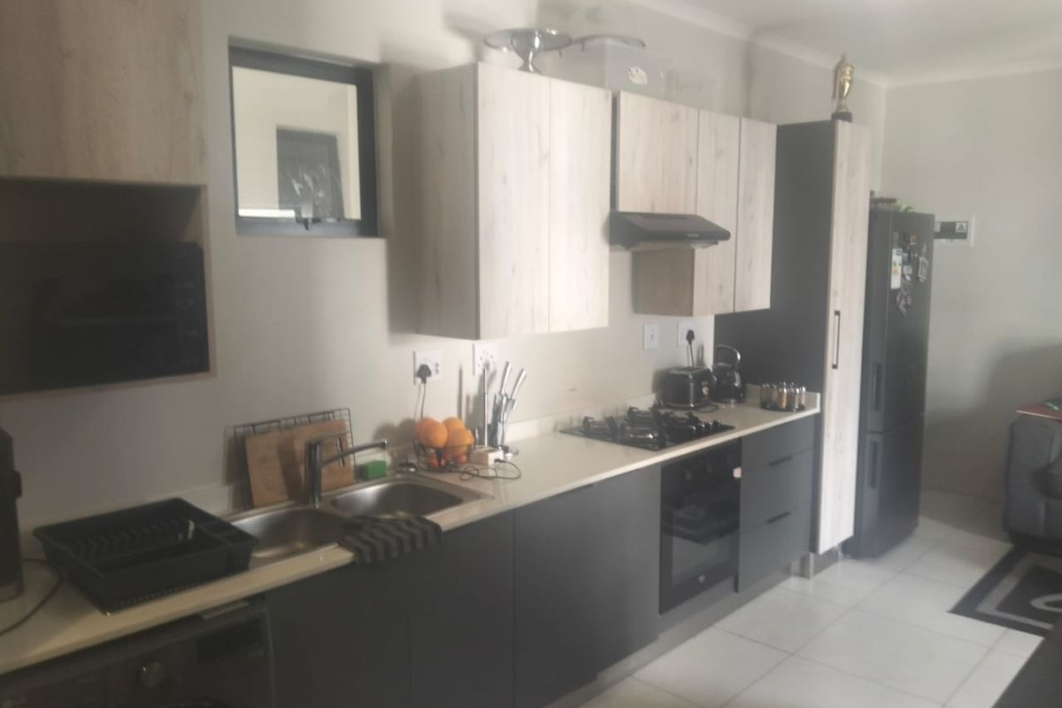 Modern kitchen featuring light wood-look upper cabinets, dark lower cabinetry, stone countertops, gas hob, built-in oven, and tiled flooring.