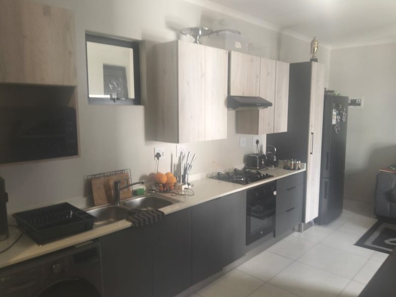 Modern kitchen featuring light wood-look upper cabinets, dark lower cabinetry, stone countertops, gas hob, built-in oven, and tiled flooring.