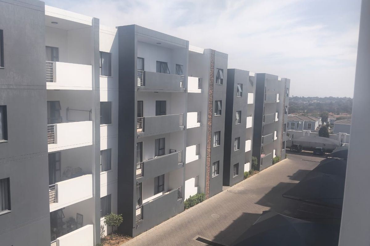 Exterior view of a modern multi-story apartment complex featuring private balconies, paved driveway, and covered parking areas.