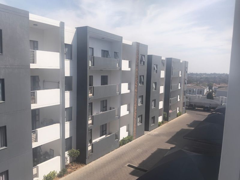Exterior view of a modern multi-story apartment complex featuring private balconies, paved driveway, and covered parking areas.