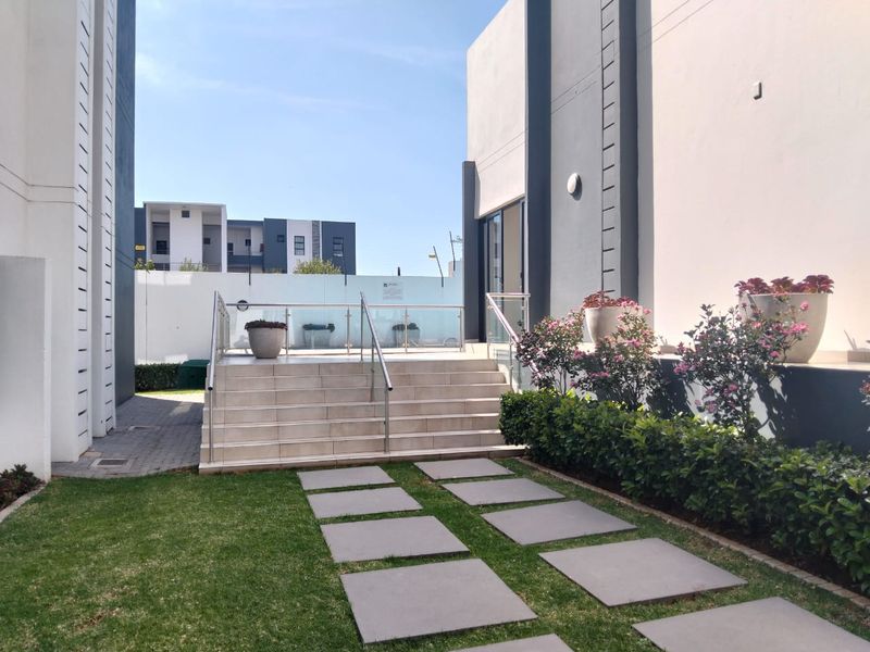 A well-maintained rear exterior area featuring a tiled staircase with glass balustrades, leading to a paved walkway and landscaped garden.