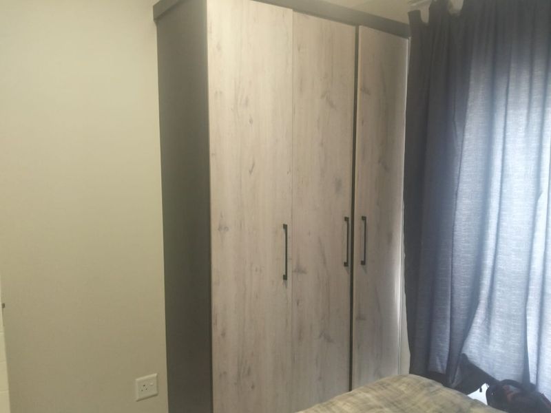 A bedroom featuring a modern, light wood-grain finish built-in wardrobe with dark trim and handles.