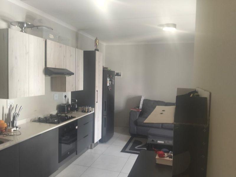 An open-plan kitchen and living area featuring modern two-tone cabinetry, a gas hob, and tiled flooring, offering a functional and contemporary layout.