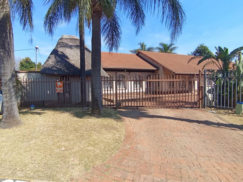 Front exterior view of the property featuring a combination of thatched and tiled roofing, a brick driveway, and secure steel perimeter fencing.