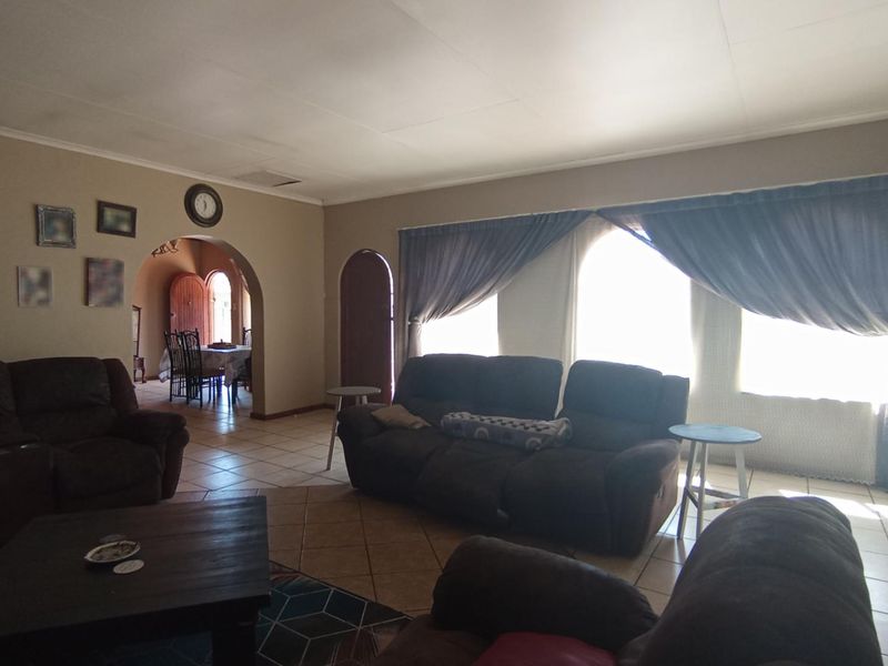 Spacious living room featuring tiled flooring, a distinctive arched doorway leading to the dining area, and large windows allowing for natural light.