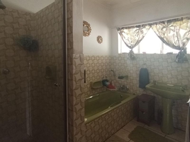 A dated bathroom featuring a built-in bathtub, pedestal basin, and separate shower enclosure with patterned wall tiling.