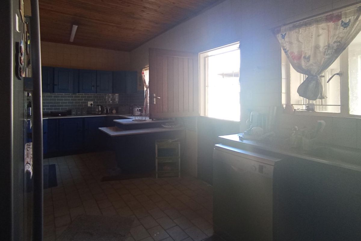 A functional kitchen featuring dark blue cabinetry, tiled flooring, and a timber ceiling, with a stable door providing access to the exterior.