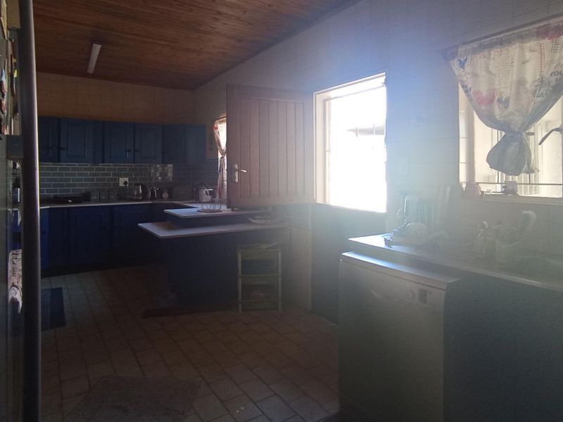 A functional kitchen featuring dark blue cabinetry, tiled flooring, and a timber ceiling, with a stable door providing access to the exterior.