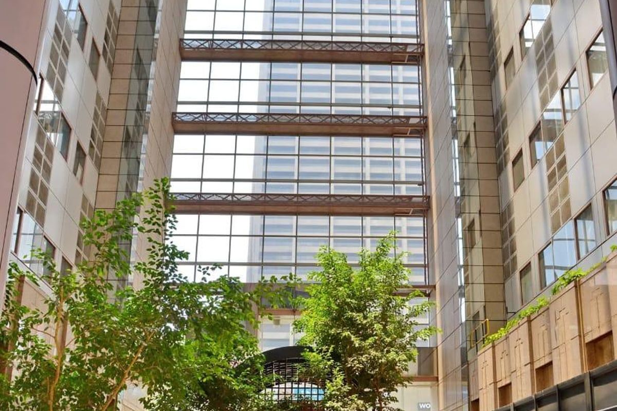 A grand, light-filled atrium entrance featuring a soaring glass ceiling, stone flooring, and integrated indoor planters within a modern apartment complex.