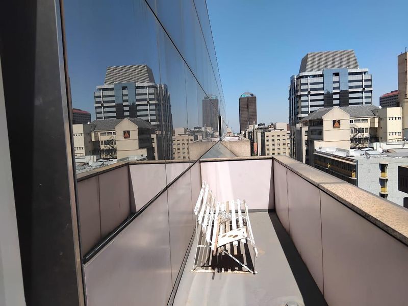 A narrow balcony featuring a glass facade and metal balustrade, offering an urban city view.
