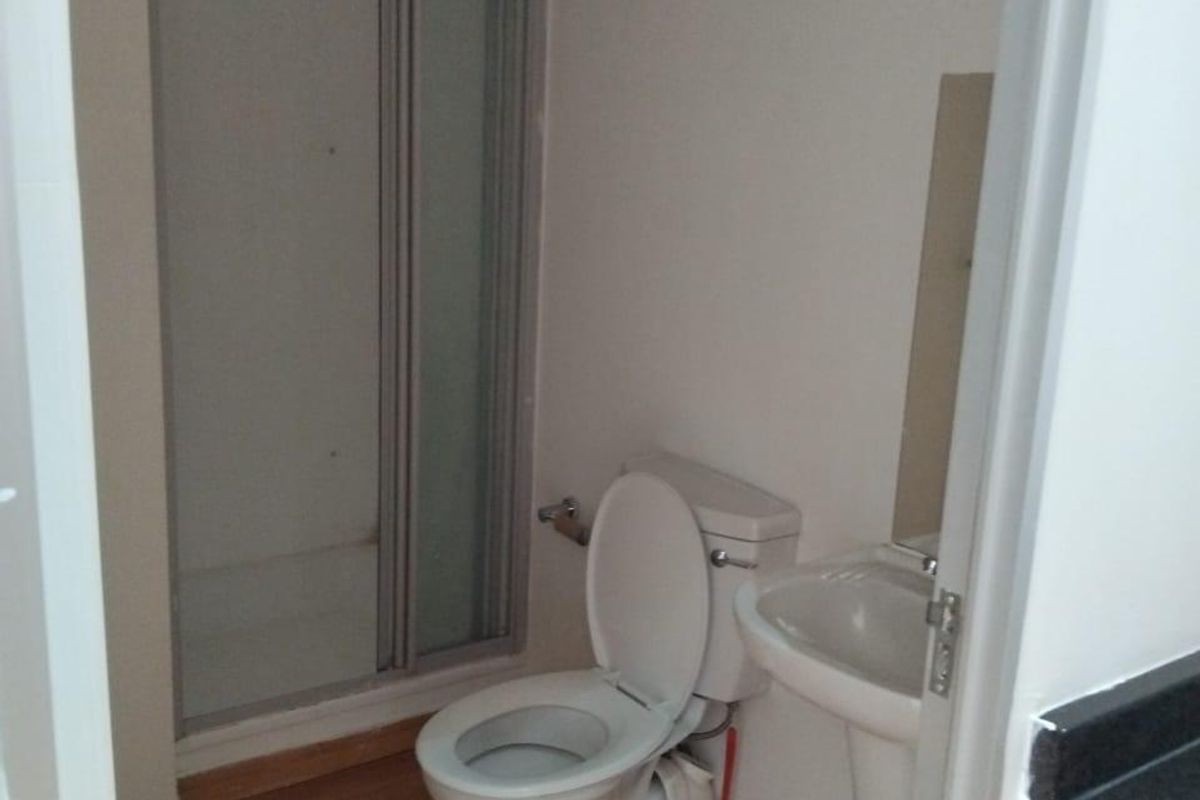 A functional bathroom featuring a shower enclosure, pedestal basin, and toilet with laminate flooring.