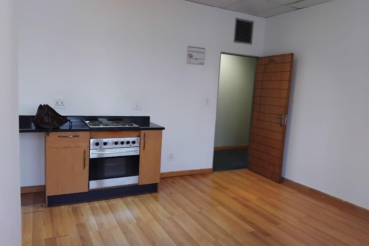 A compact kitchen area featuring a built-in oven, hob, and black granite countertop, set against a backdrop of laminate flooring and a wooden door.