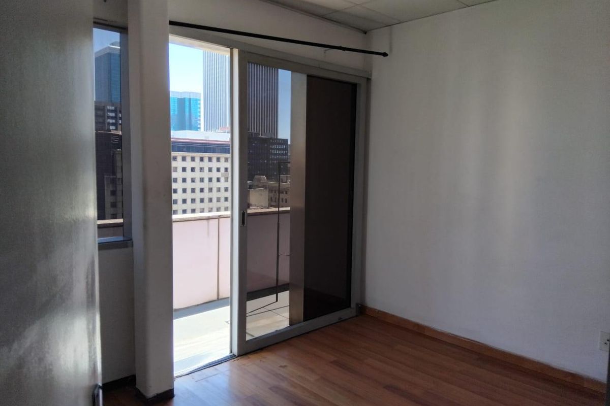 An empty bedroom featuring laminate flooring, a drop ceiling, and a sliding glass door providing access to a balcony with city views.