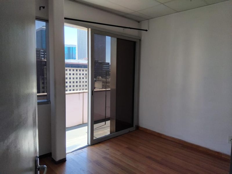 An empty bedroom featuring laminate flooring, a drop ceiling, and a sliding glass door providing access to a balcony with city views.