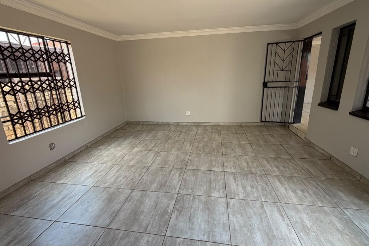 A bright, empty living room featuring neutral wall paint, modern wood-look ceramic floor tiles, and secure metal security gates on the windows and door.