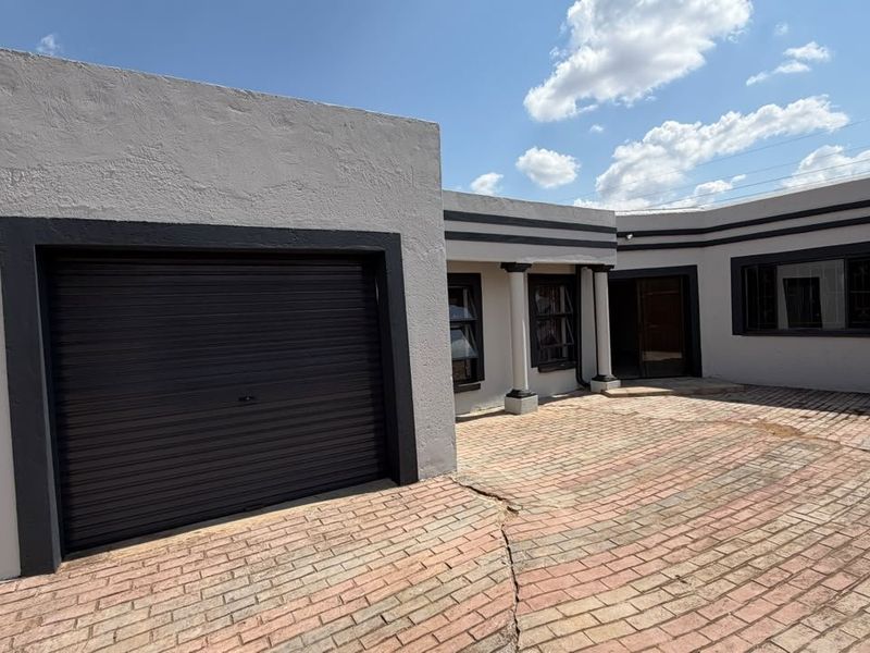 Front exterior view of the house featuring a roller garage door, paved driveway, and decorative columns.