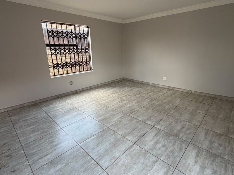 A clean, empty bedroom featuring neutral tiled flooring, coving, and secure window and door fittings.