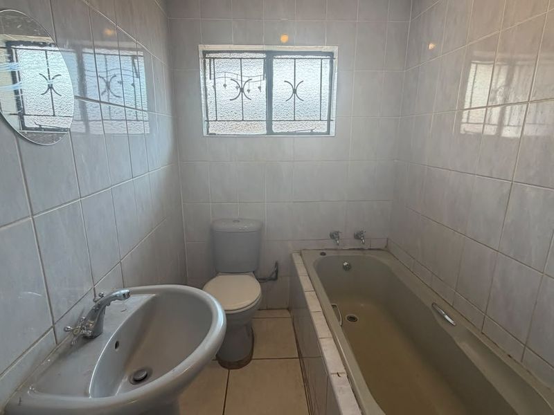 A functional bathroom featuring a pedestal basin, toilet, and built-in bathtub with full-height wall tiling and security bars on the window.