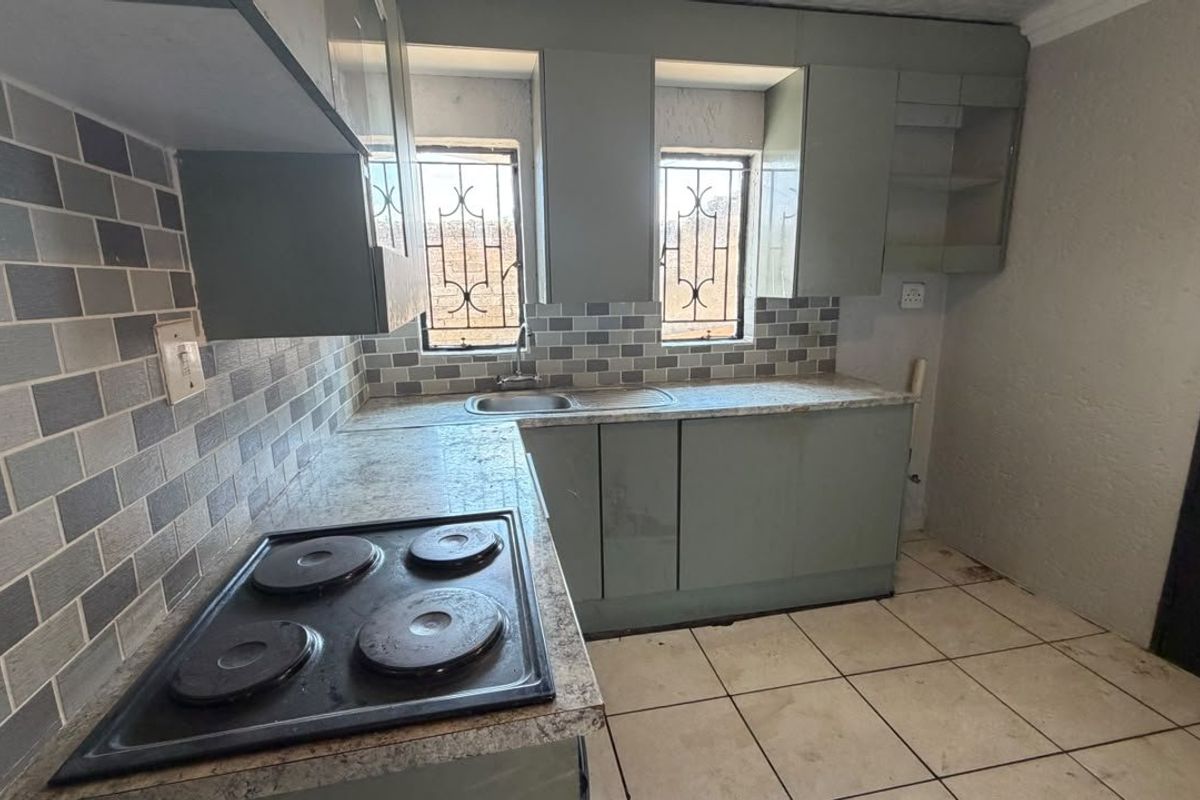 A compact kitchen featuring built-in cabinetry, a tiled backsplash, and an integrated electric hob, offering a functional space ready for modernization.