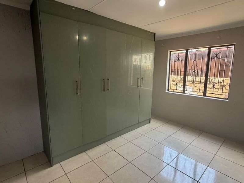 A vacant bedroom featuring large built-in wardrobes, tiled flooring, and a window fitted with security bars.