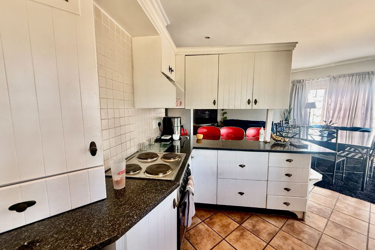 A functional kitchen featuring white cabinetry, granite countertops, an electric hob, and a breakfast bar, opening into the adjacent living area.