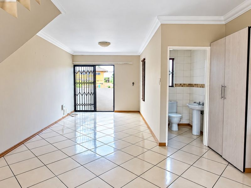 Open plan living area featuring tiled flooring, a staircase, and an adjacent guest bathroom with a pedestal basin and toilet.