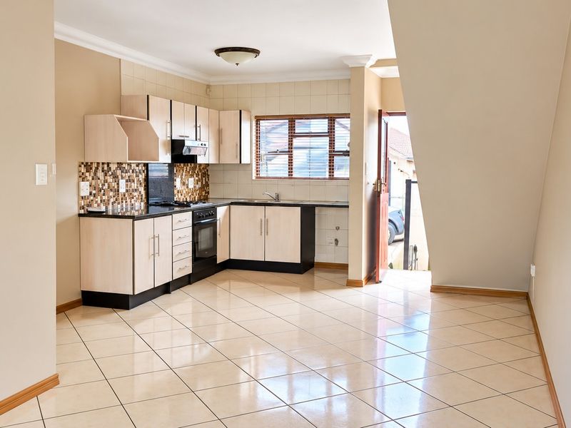 A clean, empty kitchen featuring light-toned cabinetry, dark countertops, tiled flooring, and a tiled backsplash, with direct access to the exterior.
