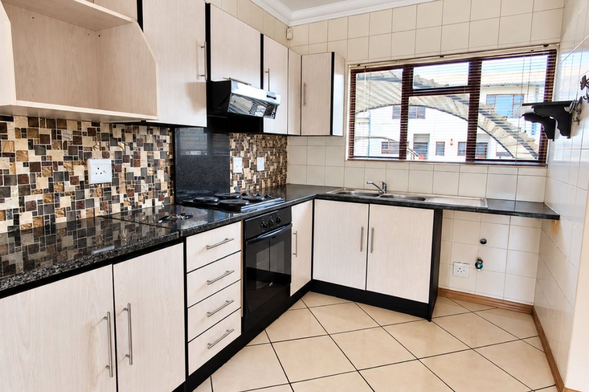 A functional kitchen featuring light wood-finish cabinetry, granite countertops, a built-in oven with gas hob, and tiled flooring throughout.