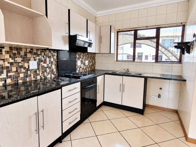 A functional kitchen featuring light wood-finish cabinetry, granite countertops, a built-in oven with gas hob, and tiled flooring throughout.